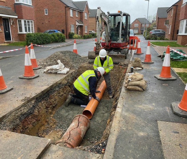 Drain repair team assessing damaged underground pipework before remedial works.